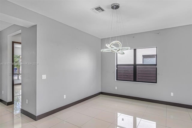 tiled spare room featuring an inviting chandelier