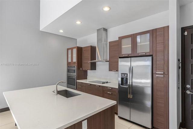 kitchen with light tile patterned flooring, wall chimney range hood, sink, appliances with stainless steel finishes, and a kitchen island with sink