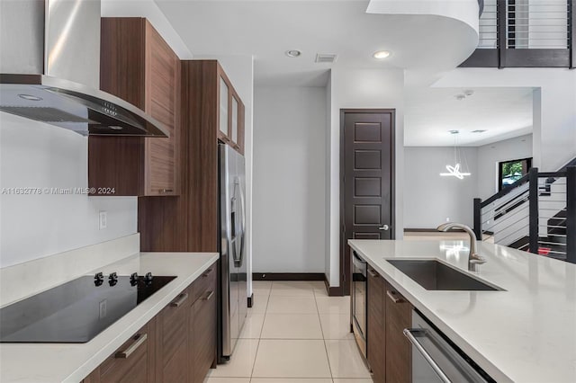 kitchen with decorative light fixtures, wall chimney exhaust hood, sink, appliances with stainless steel finishes, and light tile patterned floors