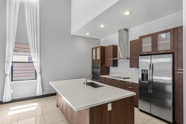 kitchen featuring stainless steel appliances, an island with sink, sink, and wall chimney range hood