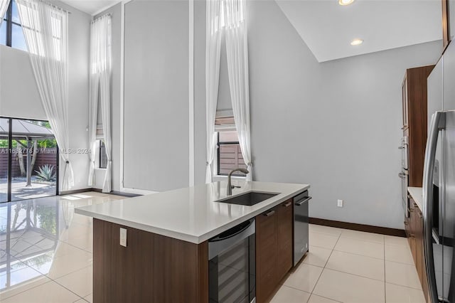 kitchen with an island with sink, sink, wine cooler, dark brown cabinetry, and light tile patterned floors