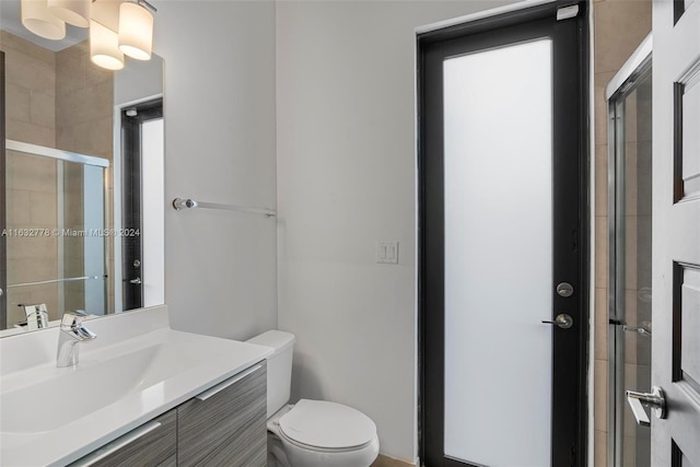 bathroom featuring a shower with door, toilet, and vanity