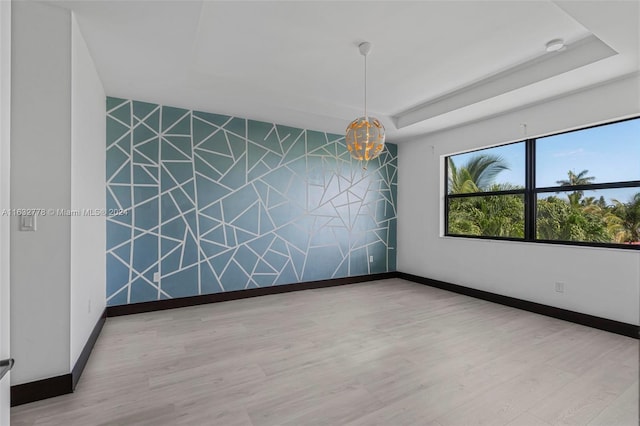 unfurnished room featuring light hardwood / wood-style floors, a notable chandelier, and a raised ceiling