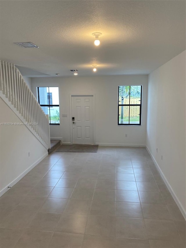 foyer featuring a healthy amount of sunlight, light tile patterned floors, visible vents, and stairway