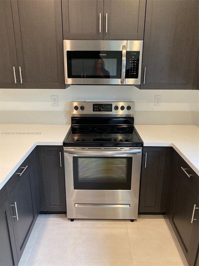 kitchen with appliances with stainless steel finishes, light tile patterned floors, and dark brown cabinetry