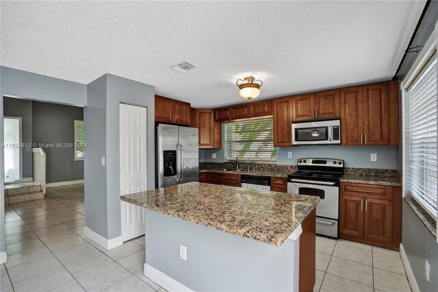 kitchen featuring stainless steel appliances, light stone counters, a kitchen island, a textured ceiling, and light tile patterned floors