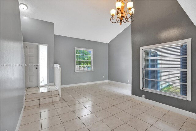 tiled empty room featuring high vaulted ceiling and a chandelier