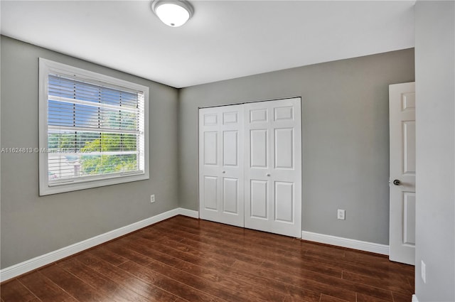 unfurnished bedroom featuring dark wood-style floors, baseboards, and a closet