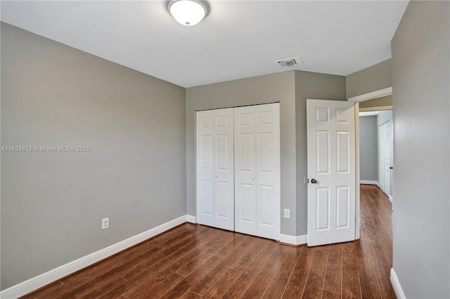 unfurnished bedroom featuring a closet, visible vents, baseboards, and wood finished floors