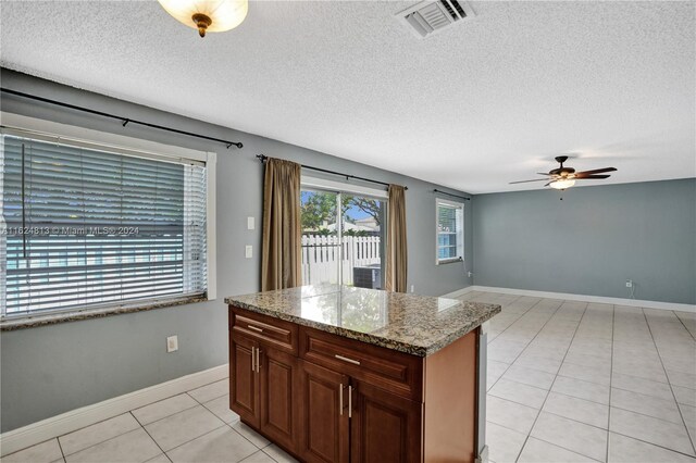 kitchen featuring light tile patterned flooring, ceiling fan, a center island, stone countertops, and a textured ceiling