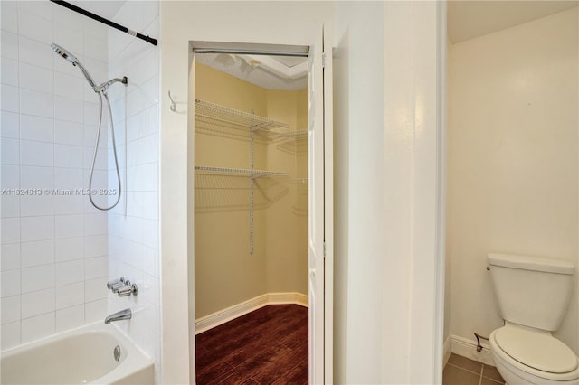 full bathroom with shower / bath combination, baseboards, toilet, wood finished floors, and a walk in closet