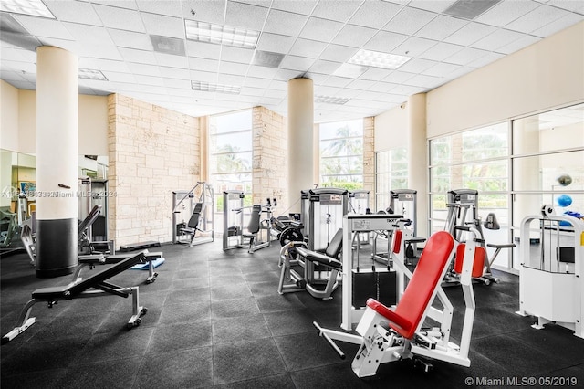 exercise room featuring floor to ceiling windows, a paneled ceiling, and a healthy amount of sunlight