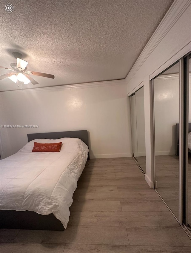 bedroom featuring crown molding, a textured ceiling, wood-type flooring, ceiling fan, and multiple closets