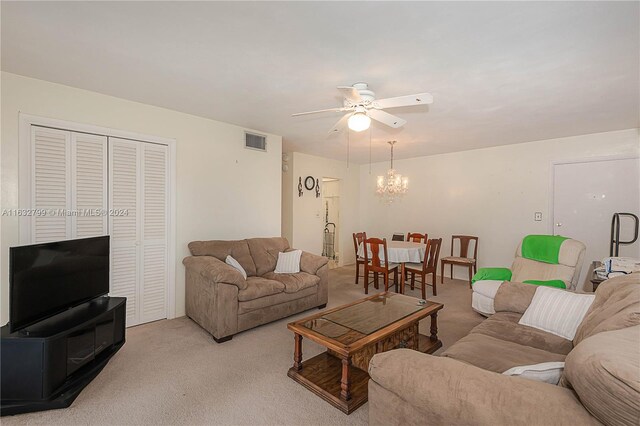 carpeted living room with ceiling fan with notable chandelier