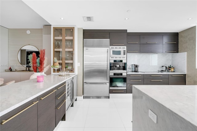 kitchen featuring backsplash, built in appliances, light tile patterned floors, and light stone counters