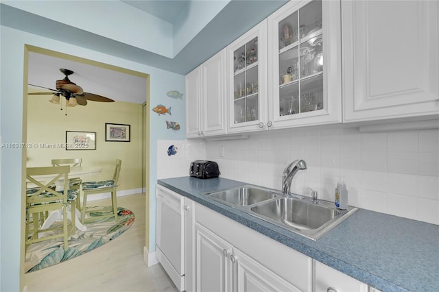kitchen with white dishwasher, a sink, tasteful backsplash, glass insert cabinets, and white cabinetry