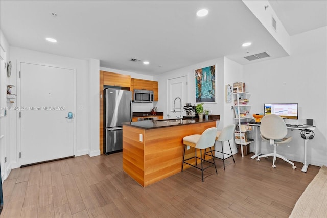 kitchen with appliances with stainless steel finishes, a breakfast bar, sink, kitchen peninsula, and light wood-type flooring