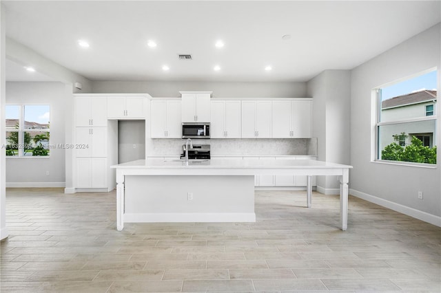 kitchen featuring stove, decorative backsplash, white cabinets, and an island with sink