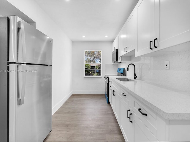 kitchen featuring light hardwood / wood-style flooring, white cabinets, stainless steel appliances, light stone countertops, and sink