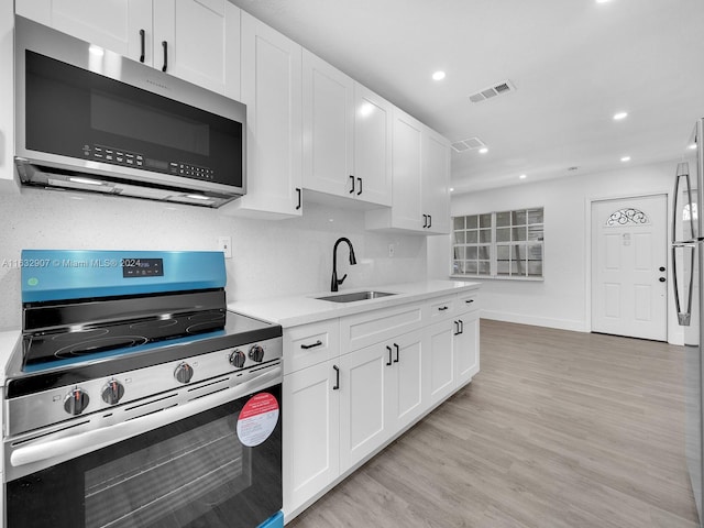 kitchen with stainless steel appliances, white cabinets, sink, light stone counters, and light hardwood / wood-style floors