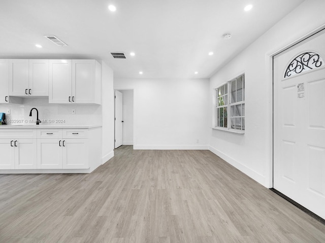 kitchen with white cabinetry, sink, light hardwood / wood-style floors, and decorative backsplash