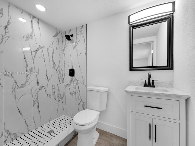 bathroom with wood-type flooring, tiled shower, vanity, and toilet