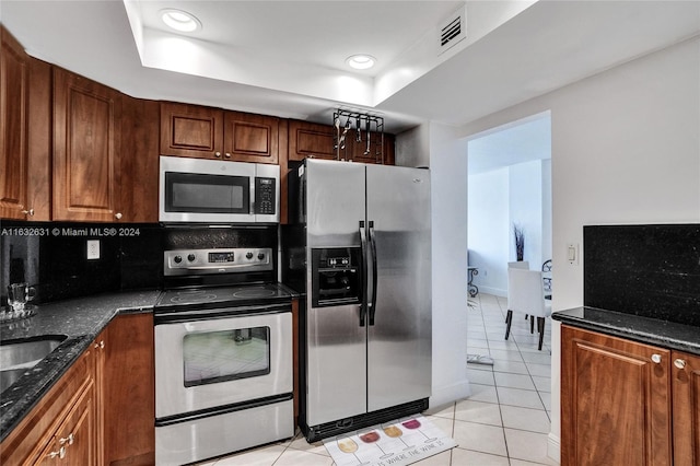 kitchen with light tile patterned flooring, dark stone countertops, decorative backsplash, and stainless steel appliances