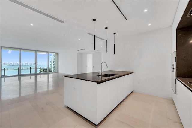 kitchen with light tile patterned flooring, white cabinetry, floor to ceiling windows, pendant lighting, and sink