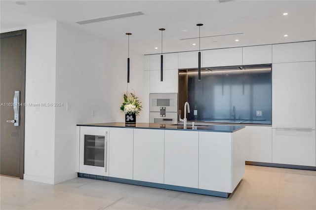 kitchen with white cabinetry, beverage cooler, hanging light fixtures, sink, and a center island with sink