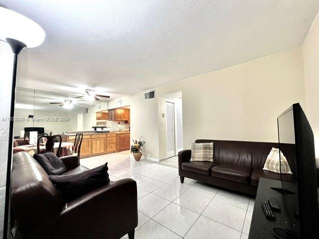 living room with ceiling fan, a textured ceiling, and light tile patterned floors