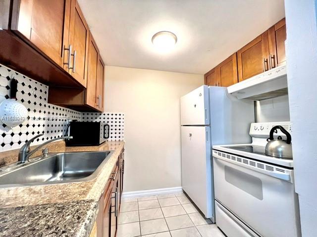 kitchen featuring white appliances, backsplash, stone counters, light tile patterned floors, and sink