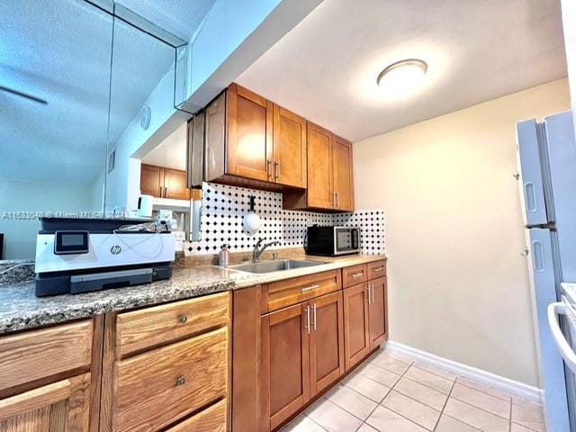 kitchen featuring light tile patterned flooring, dark stone countertops, backsplash, stainless steel fridge, and sink