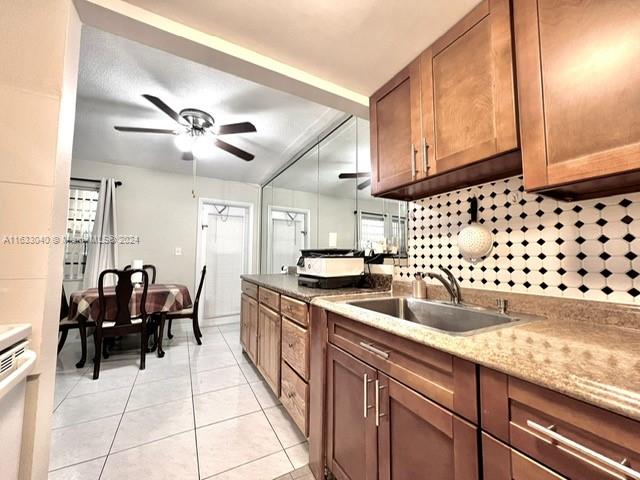 kitchen featuring light tile patterned floors, ceiling fan, sink, backsplash, and light stone counters