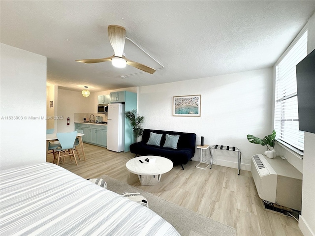 bedroom with a textured ceiling, ceiling fan, an AC wall unit, freestanding refrigerator, and light wood finished floors