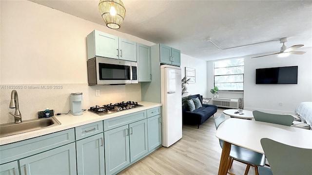 kitchen featuring stainless steel appliances, a sink, a ceiling fan, light wood-style floors, and light countertops