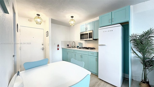 kitchen featuring stainless steel appliances, light countertops, a sink, a textured ceiling, and light wood-type flooring