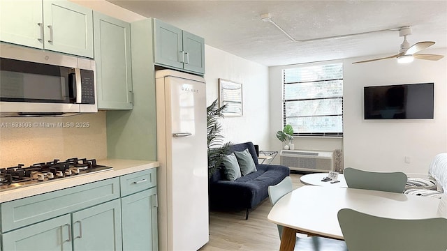 kitchen with a ceiling fan, stainless steel appliances, light countertops, light wood-type flooring, and green cabinetry