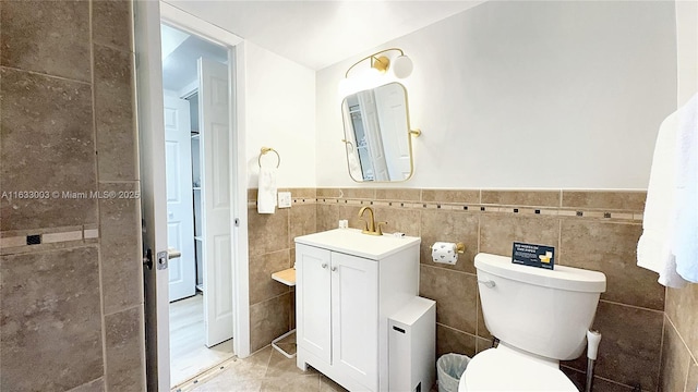 bathroom with wainscoting, toilet, tile patterned floors, vanity, and tile walls