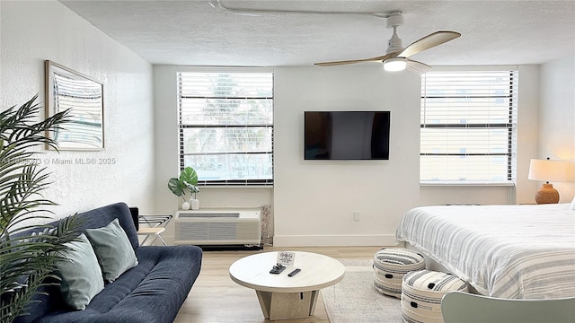 bedroom featuring light wood-type flooring, a textured ceiling, an AC wall unit, and a textured wall