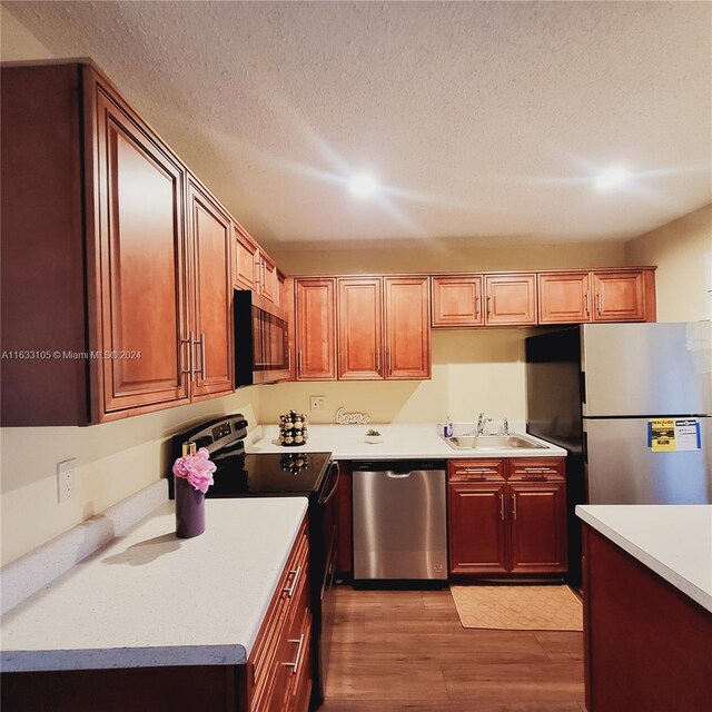 kitchen with sink, light wood-type flooring, a textured ceiling, and stainless steel appliances