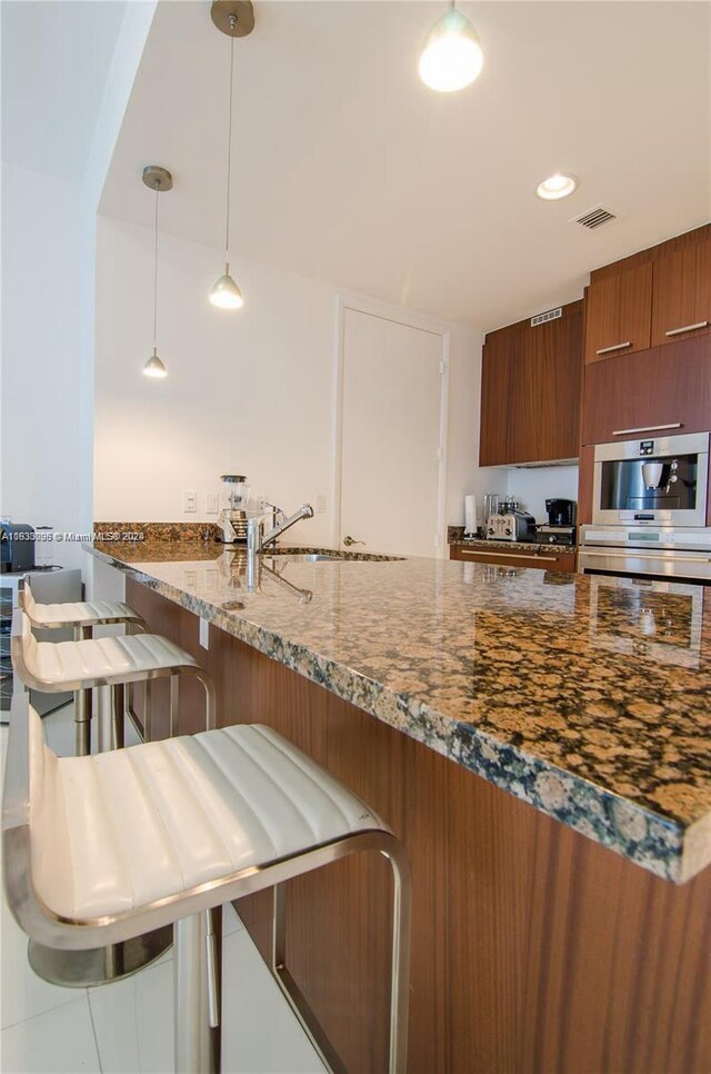 kitchen with decorative light fixtures, sink, a kitchen bar, stone countertops, and kitchen peninsula