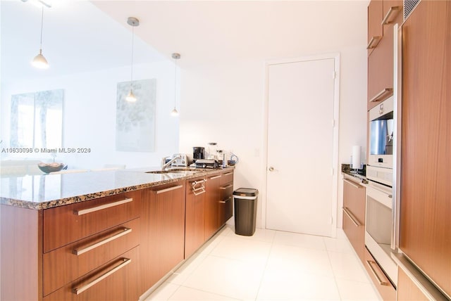 kitchen with sink, light stone counters, hanging light fixtures, light tile patterned flooring, and high quality fridge