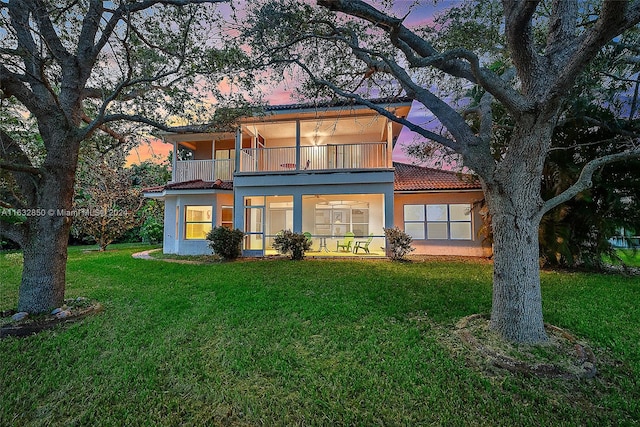 back house at dusk featuring a balcony and a yard