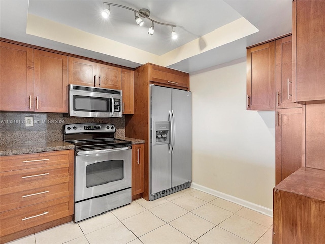 kitchen featuring stainless steel appliances, tasteful backsplash, light tile patterned flooring, and a tray ceiling