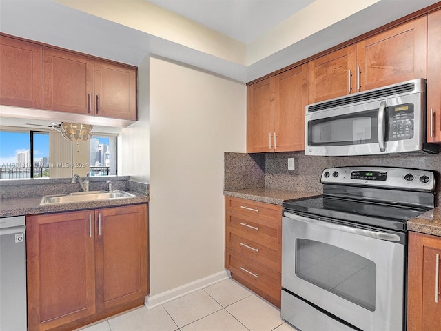 kitchen with sink, light tile patterned floors, appliances with stainless steel finishes, dark stone countertops, and decorative backsplash