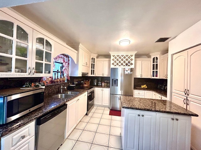 kitchen featuring sink, backsplash, white cabinetry, stainless steel appliances, and dark stone countertops