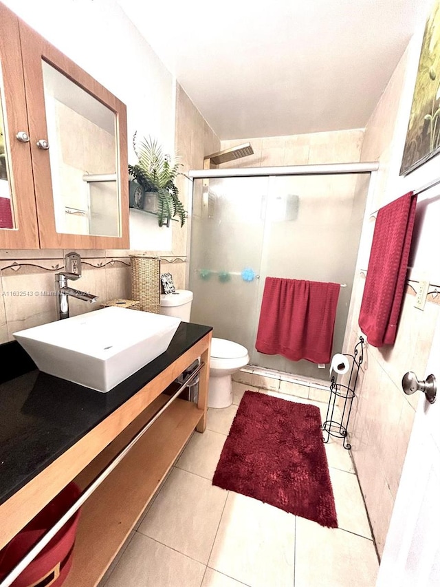 bathroom featuring vanity, a shower with shower door, tile patterned floors, tile walls, and toilet