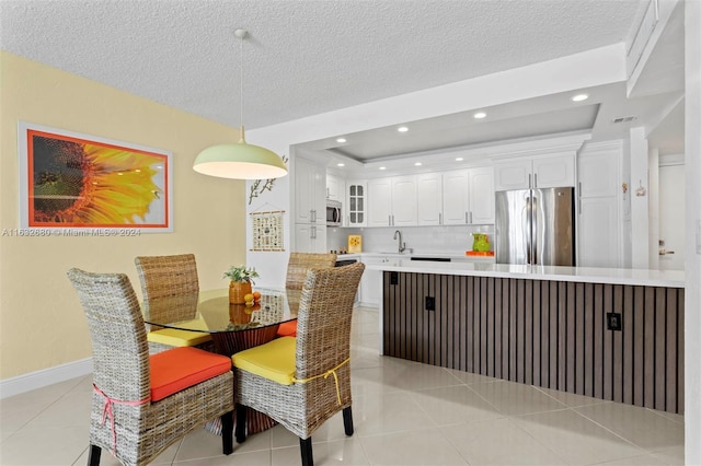 dining area featuring a tray ceiling, sink, light tile patterned floors, and a textured ceiling