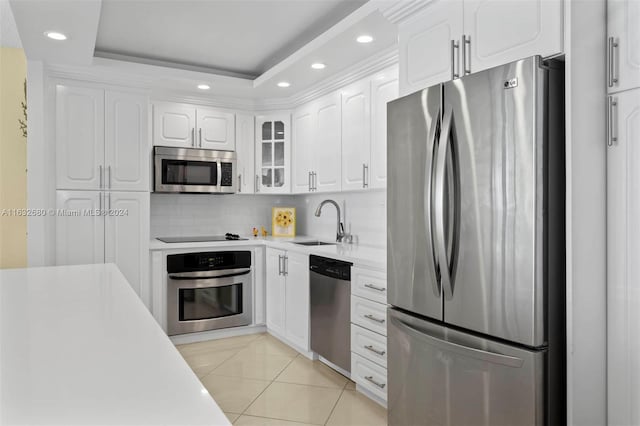 kitchen with light tile patterned flooring, appliances with stainless steel finishes, white cabinetry, sink, and a raised ceiling