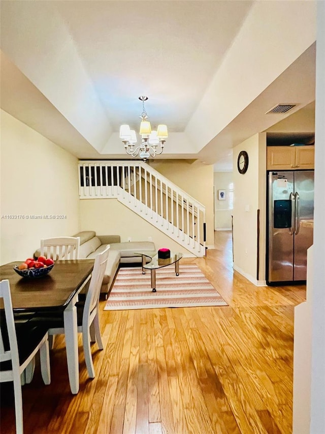 dining space featuring a raised ceiling, a chandelier, and light hardwood / wood-style floors